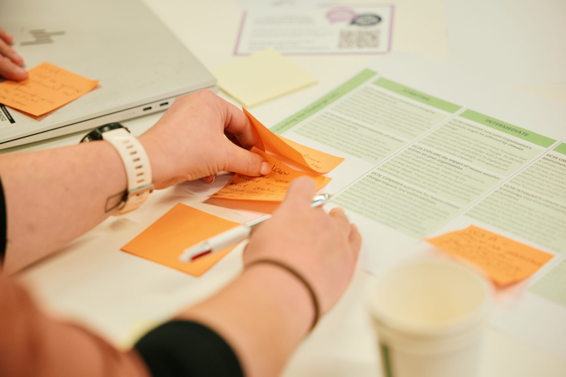 Photo of someone writing on a post-it note, showing their hands and a coffee cup